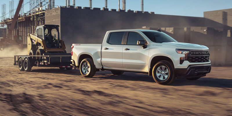 White Chevrolet Silverado towing construction equipment.